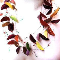 a woman wearing a necklace made out of leaves and beaded with red, green, yellow and orange beads