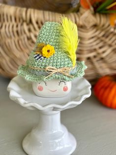 a crocheted green hat with yellow feathers on top of a white cake plate