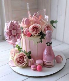 a pink cake with roses and macaroons on it, next to a bottle of champagne