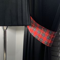 a red and green plaid tie hanging on a black curtain next to a light fixture