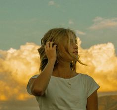 a woman talking on her cell phone while standing in front of a mountain with clouds