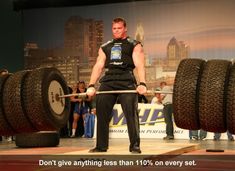 a man holding a barbell on top of a wooden platform in front of a crowd