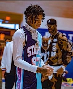 two young men standing next to each other in front of a basketball court, one with dreadlocks on his head