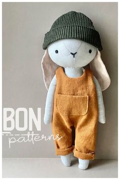 a stuffed animal wearing overalls and a green hat on top of a white wall