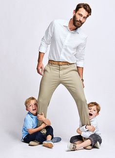 a man standing on top of two small boys in front of a white wall with his mouth open