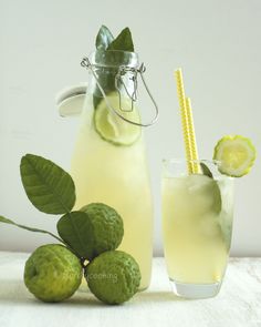 a pitcher of lemonade next to some limes and a glass with a straw