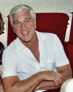 an older man and woman sitting next to each other on a red chair with their arms crossed