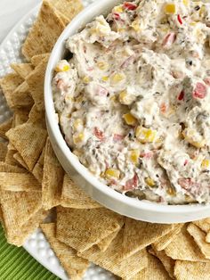 a white bowl filled with corn and dip surrounded by tortilla chips