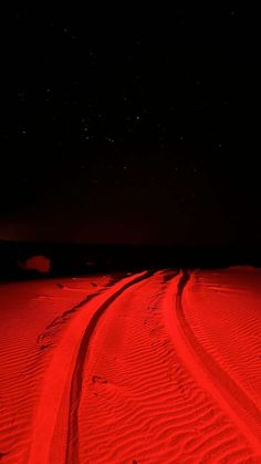 two tracks in the sand at night with bright red light shining on them and stars above