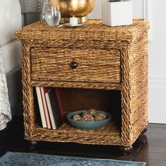 a wicker side table with a bowl and books on it next to a vase