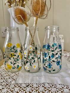 three glass vases sitting on top of a table covered in doily and flowers