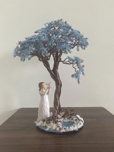 a figurine is standing next to a blue tree on a wooden table with white walls