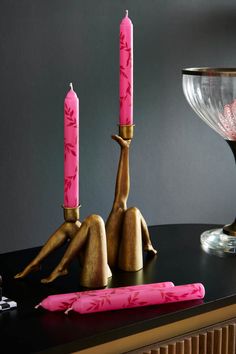 two pink candles sitting on top of a table next to a vase and candle holder