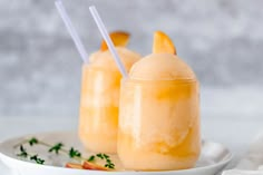 two glasses filled with orange juice and garnished with sliced peaches on a white plate