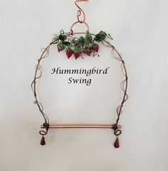 a sign that says hummingbird swing hanging from a wire with berries and leaves on it