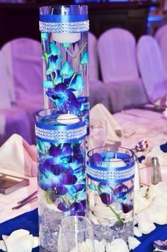 two tall vases filled with blue flowers on top of a table