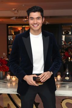 a man in a tuxedo is holding a glass and smiling at the camera