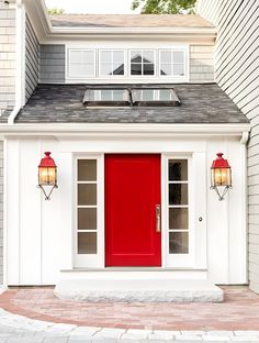 a red front door with two lights on the side of it and a white house