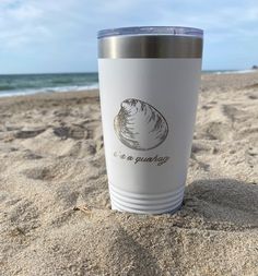 a white cup sitting on top of a sandy beach