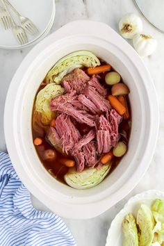 a white bowl filled with meat and vegetables on top of a marble table next to silverware