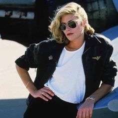 a woman in sunglasses leaning on the edge of an airplane with her hand on her hip