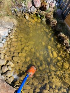 an orange and blue pipe is in the middle of some rocks near a pond that has water coming out of it