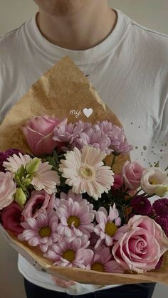 a man holding a bouquet of pink and white flowers in front of his face with the words i love you written on it