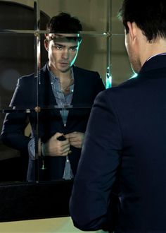 a man in a suit looking at himself in the mirror while he is adjusting his tie