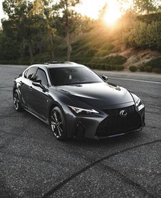 the front end of a black sports car parked in a parking lot with trees and bushes behind it