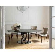 a glass table with chairs around it in front of a white wall and chandelier