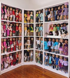 a room filled with lots of dolls on top of white bookshelves next to a wooden floor