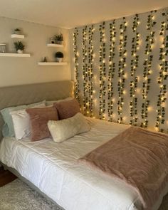 a white bed topped with lots of pillows next to a wall covered in christmas lights