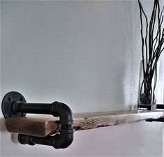 a wooden shelf with two black pipe handles and some branches in the corner behind it