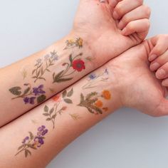 two people with tattoos on their arms are holding each other's hands and both have flowers painted on them