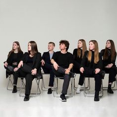 five people sitting on chairs in front of a white wall with one person looking up at the sky