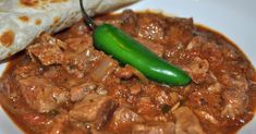 a white plate topped with meat and a green hot pepper next to a burrito