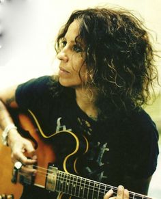 a woman with curly hair playing an acoustic guitar