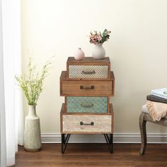 a stack of drawers sitting on top of a wooden floor next to a vase with flowers