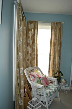 a white wicker chair sitting next to a window in a room with blue walls