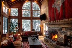 a living room with large windows and a fire place in the center is decorated with red curtains