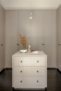 a white cabinet with two bowls on top and flowers in vases at the bottom