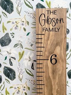 a wooden ruler with the name gibson family engraved on it, next to a floral wallpaper