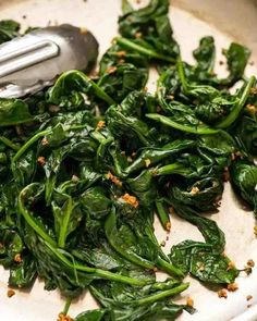 spinach being prepared in a white bowl with a metal spoon on the side and seasoning sprinkles on top