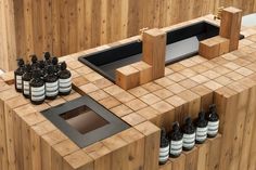 a wooden counter topped with lots of bottles next to a sink and toilet paper dispenser