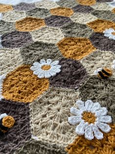 a crocheted blanket with white and brown flowers on it, sitting on top of a bed