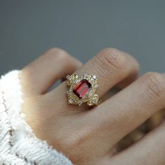 a woman's hand wearing a ring with a red stone surrounded by white diamonds