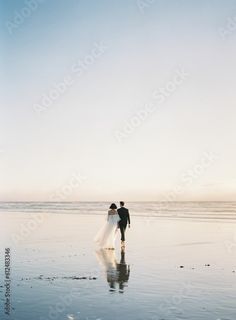 a bride and groom walking on the beach