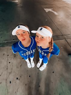 two girls in baseball uniforms are posing for the camera with their heads tilted to the side