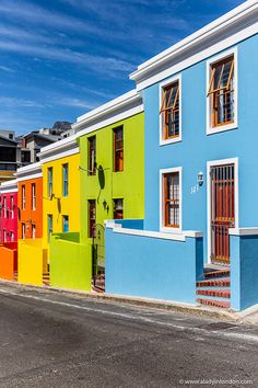 a row of multicolored buildings on the side of a street in front of a blue sky