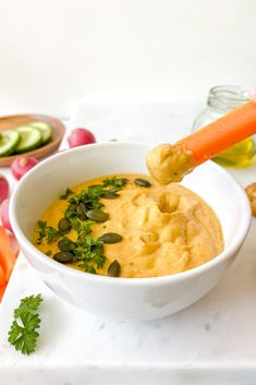 a white bowl filled with hummus, carrots and celery next to crackers